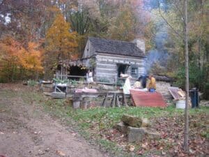 Rustic log cabin surrounded by autumn foliage and people engaged in outdoor activities.