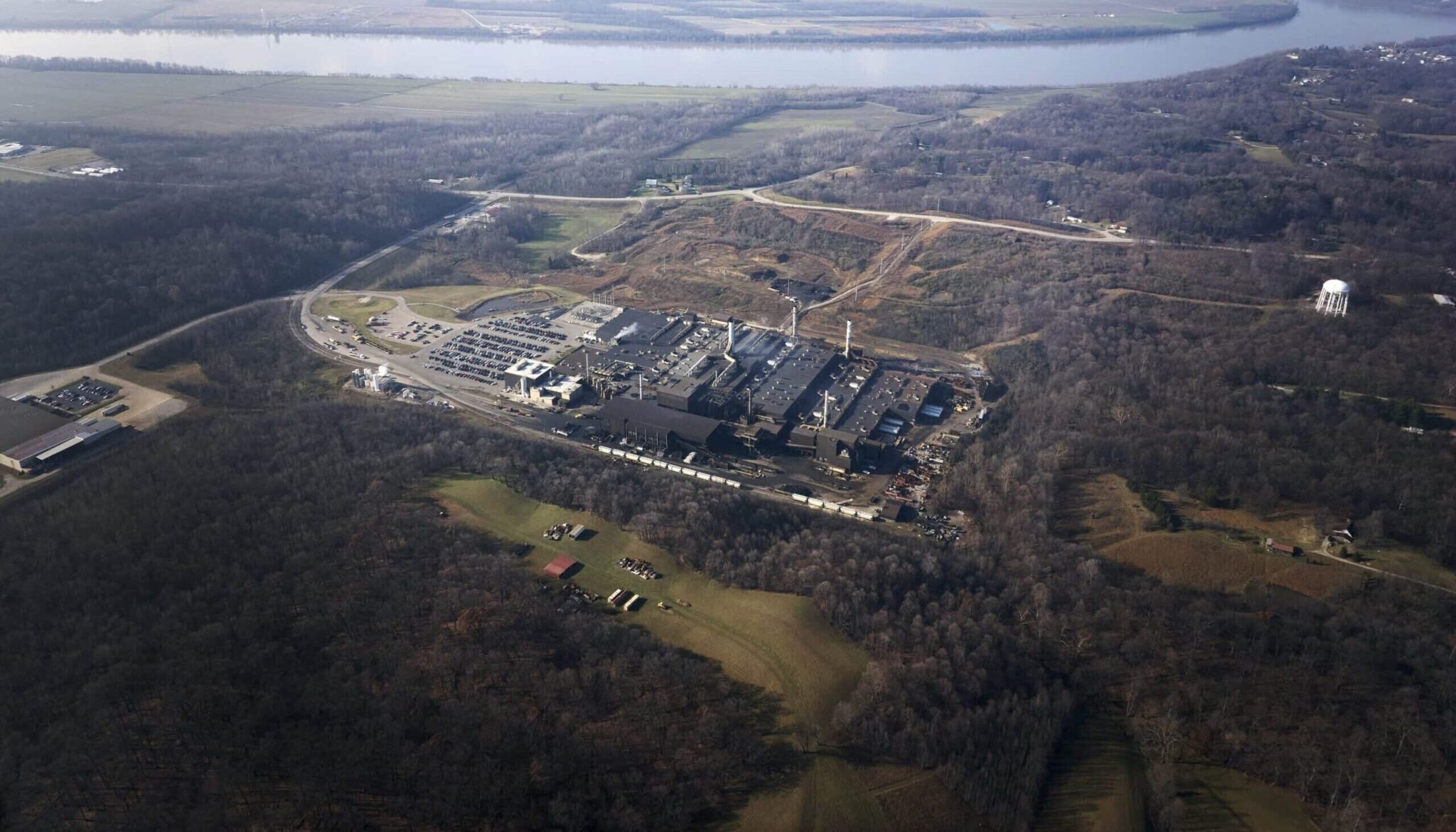 Aerial view of a factory surrounded by forests and fields near a river.