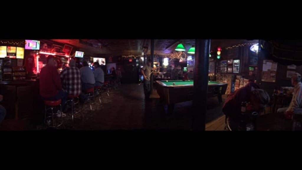 Cozy bar scene at night with patrons enjoying drinks and playing pool.
