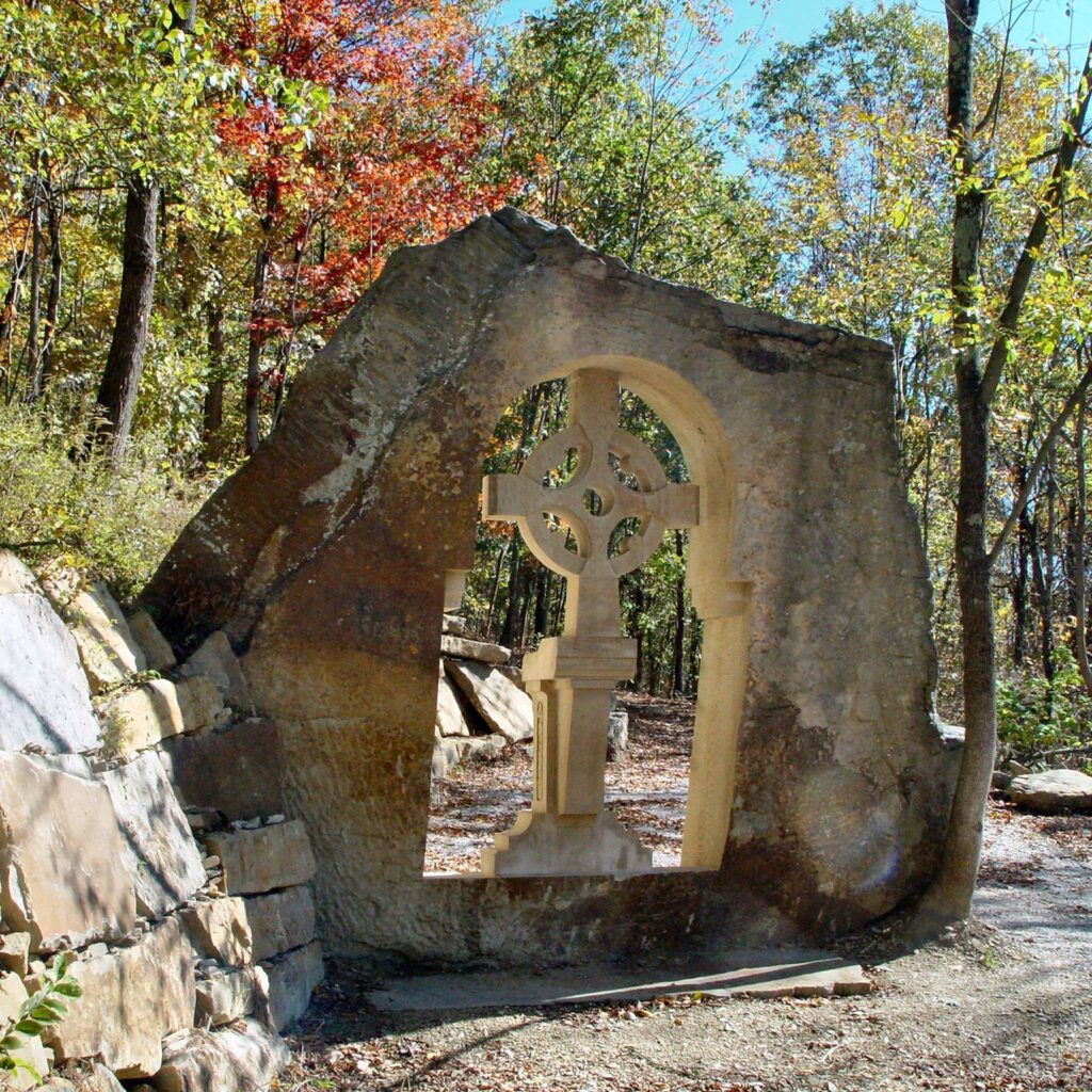 Celtic cross framed by natural stone in a serene forest setting.