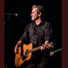 Guitarist performing live on stage with an acoustic guitar.
