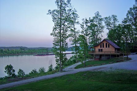 Scenic sunset view of a lakefront cabin surrounded by trees.