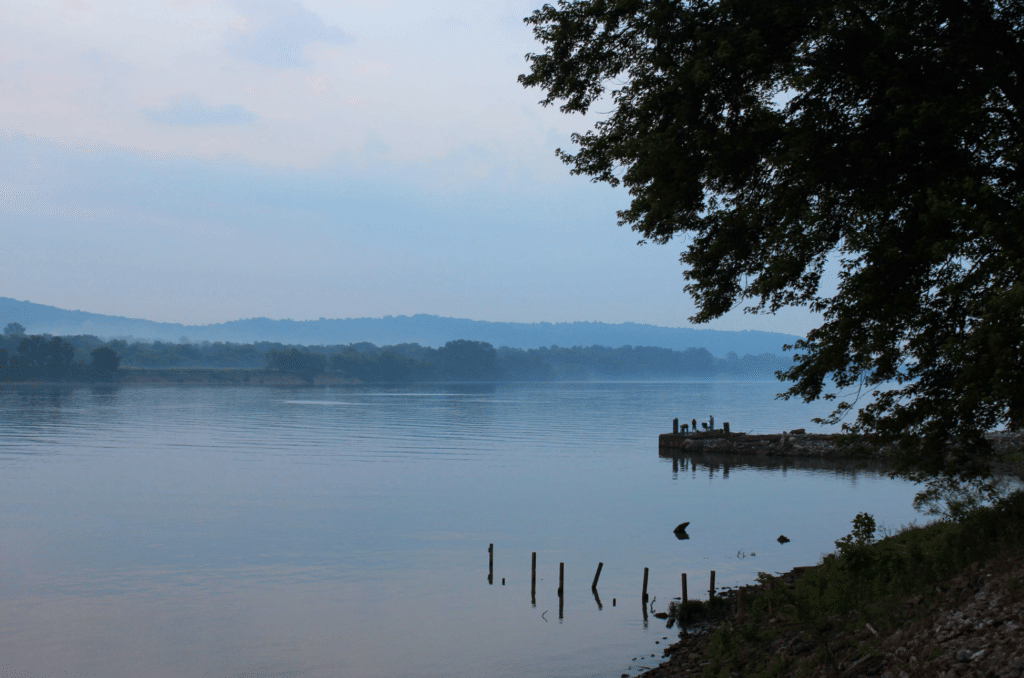 Misty river morning scene with calm waters and silhouettes of trees on the shore.