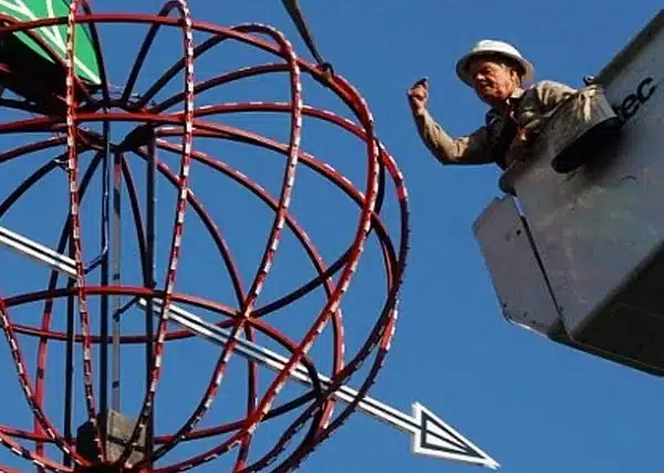 Worker repairing a sign while using a cherry picker under a clear blue sky.