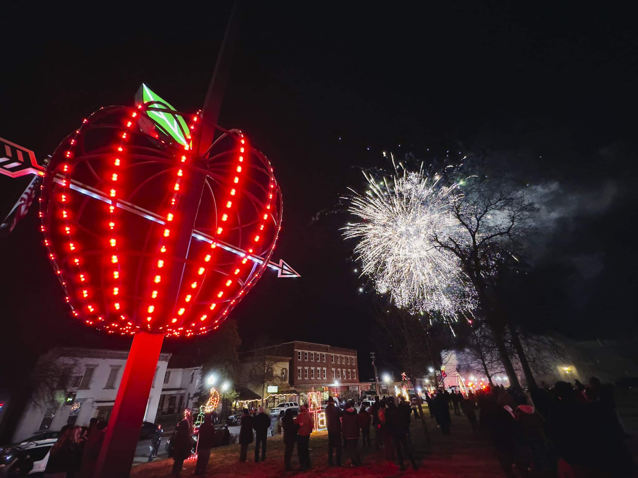 Red apple lights illuminate a fireworks display at night, creating a festive atmosphere.