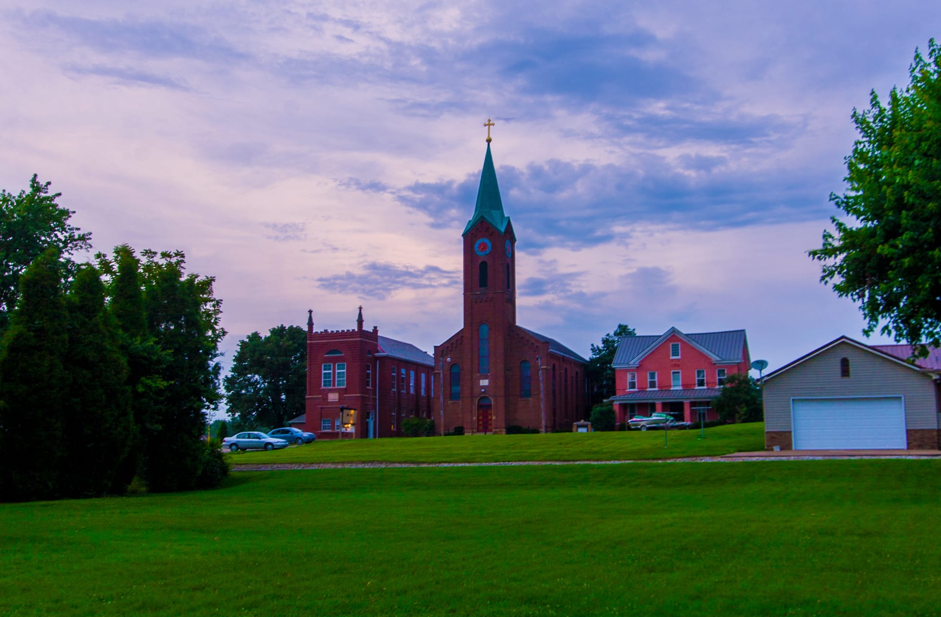 Charming St. Pius church in Troy, Indiana at sunset surrounded by lush green grass and serene skies.