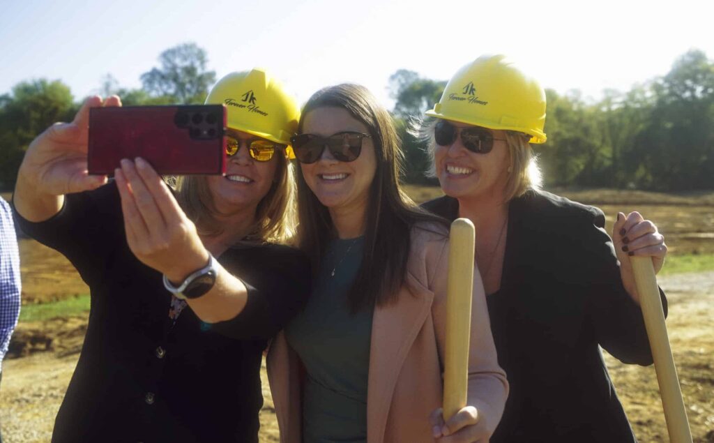 Women in yellow hardhats take a groundbreaking selfie at a construction site.