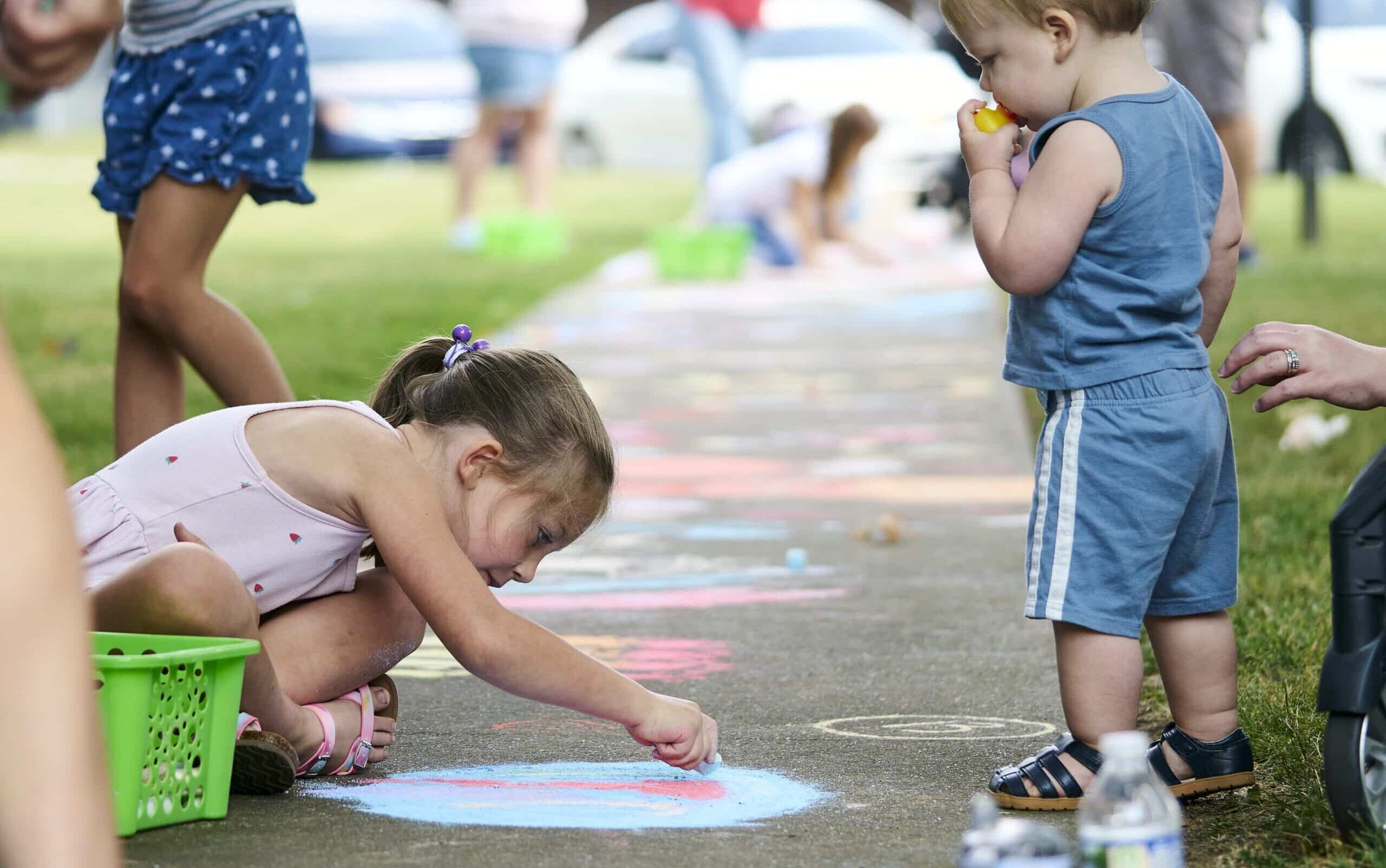 Children happily drawing with chalk on a sidewalk during a fun outdoor event.
