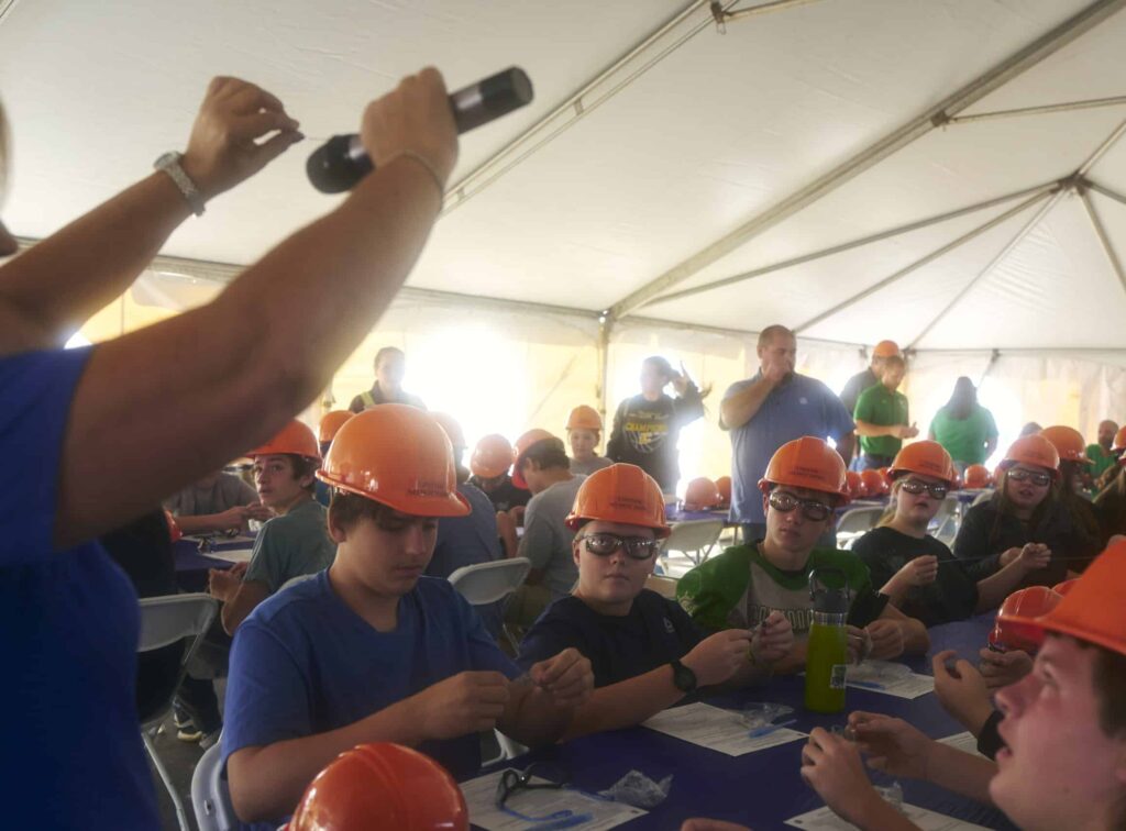 Students engaged in a hands-on learning experience inside a tent wearing safety gear.