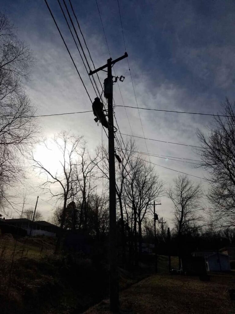 Silhouette of a power pole against a cloudy sky with overhead power lines.