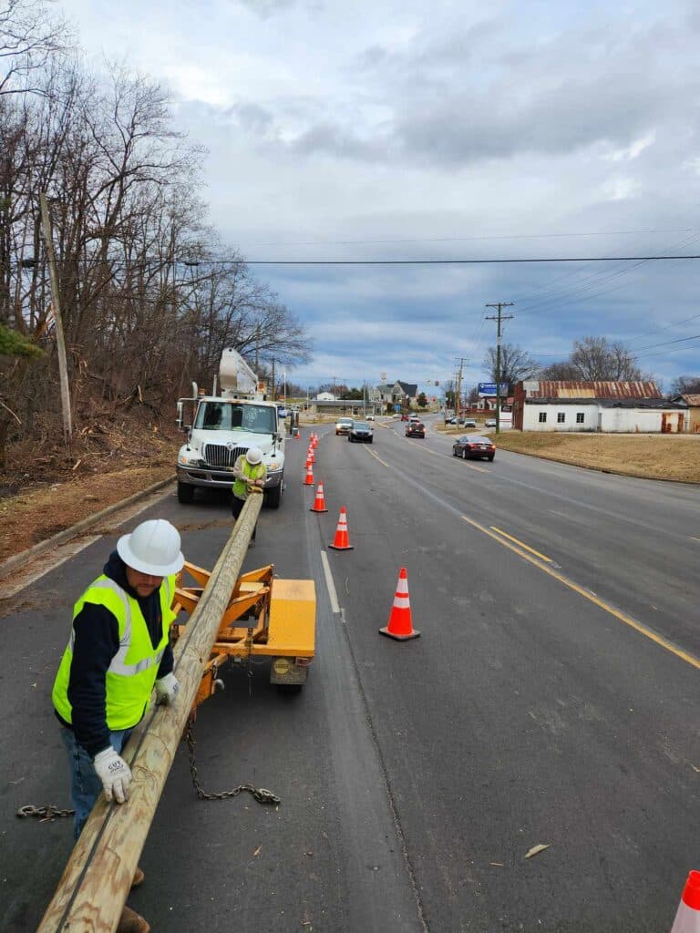 Construction crew installing utility poles on a busy road with safety cones.