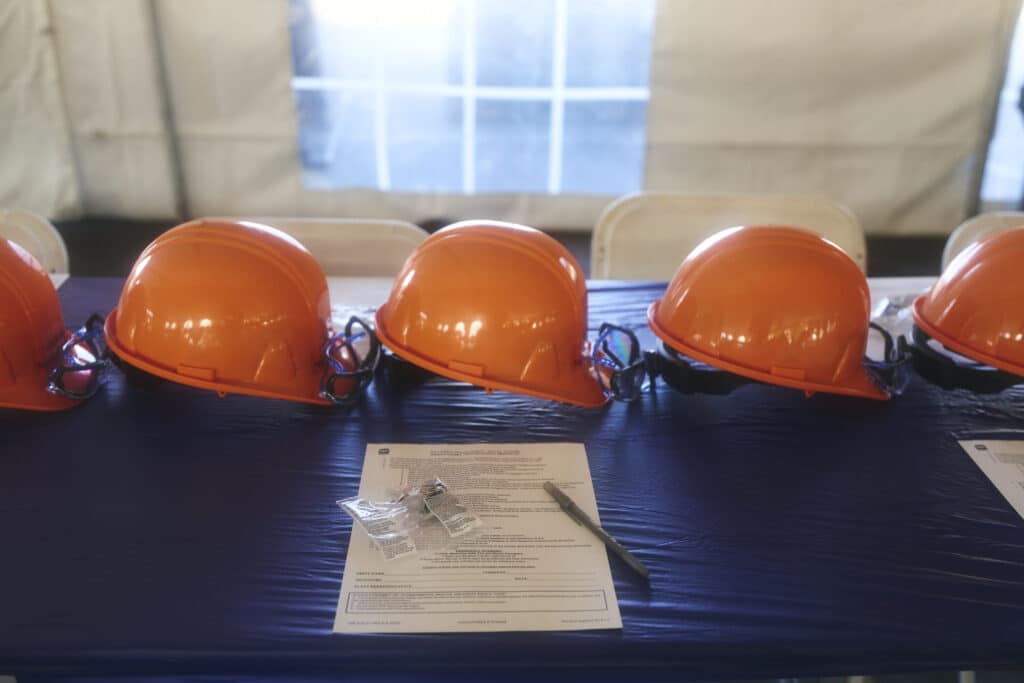 Orange safety helmets arranged on a table with paperwork and a pen.