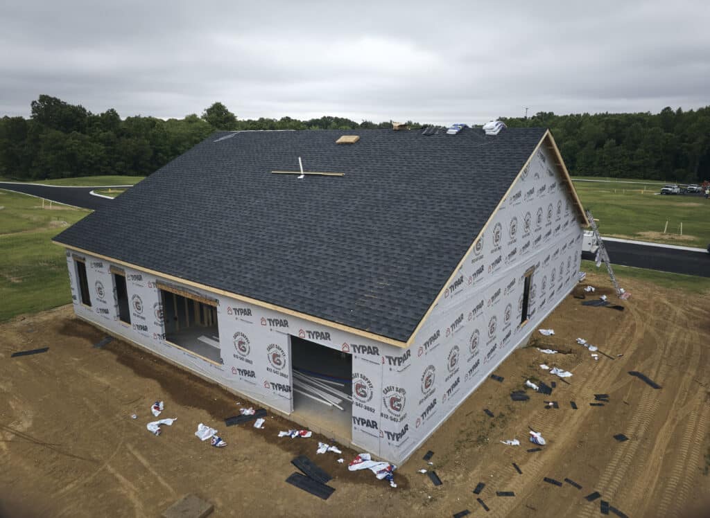 Newly constructed house with roofing materials and exterior wrapping in progress.