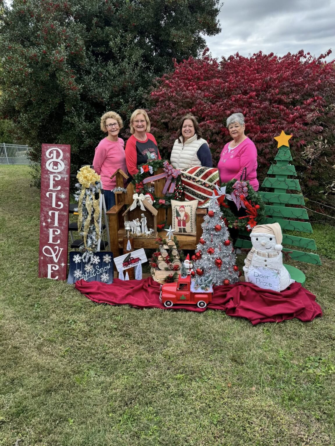 Joyful women celebrate Christmas with a festive display featuring holiday decorations and a Believe sign.