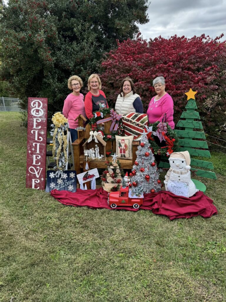 Joyful women celebrate Christmas with a festive display featuring holiday decorations and a Believe sign.