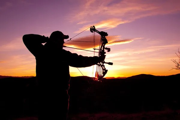 Archer silhouetted against a vibrant sunset in a beautiful outdoor setting.